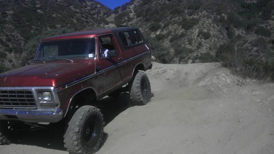 Red 1978 Ford Bronco with lifted suspension and off-road tires on a dirt trail