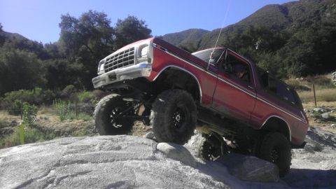 1978 Ford Bronco - This red 1978 Ford Bronco is shown navigating a rocky terrain, highlighting its off-road capabilities.