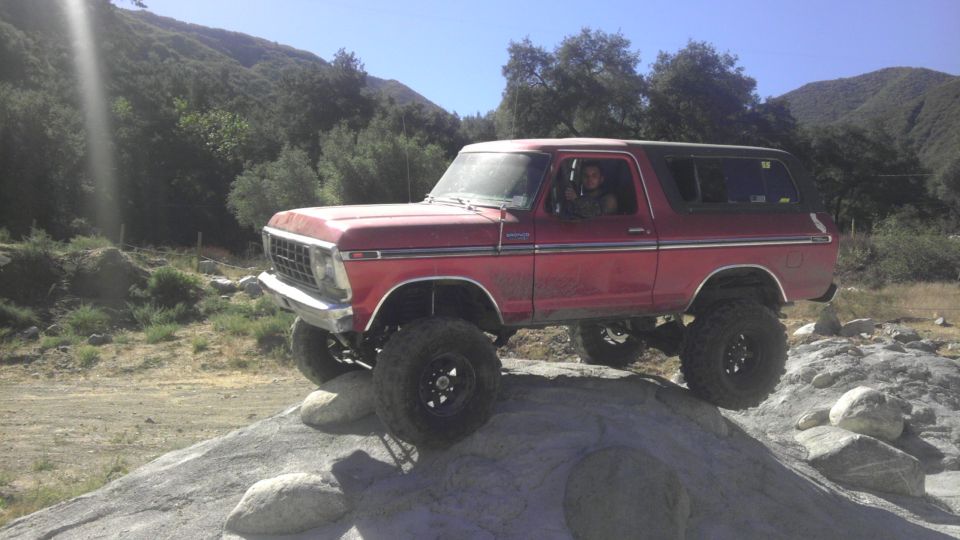 Red 1978 Ford Bronco with lifted suspension and large tires on a rocky incline