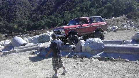 1978 Ford Bronco - A red 1978 Ford Bronco navigates a rocky off-road course with a person watching.