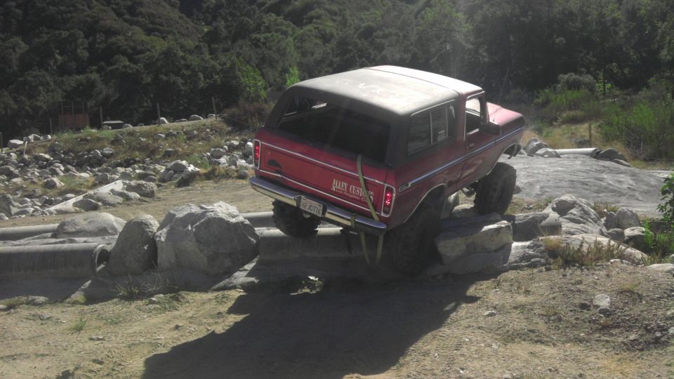 Red 1978 Ford Bronco with lifted suspension navigating rocks on an off-road trail