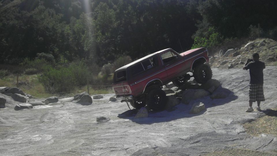 Red 1978 Ford Bronco climbing over rocks, with a person taking a photo