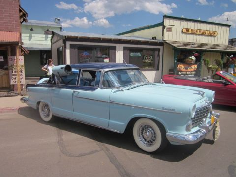 1991 Ford LTD Crown Victoria - A classic light blue sedan with a unique roof-mounted exhaust pipe is parked on a street in front of the Iron Horse Saloon.