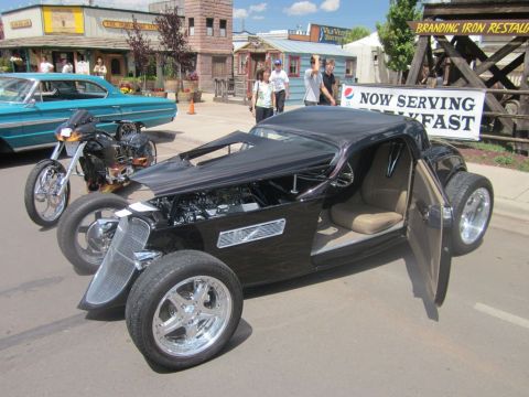 1991 Ford LTD Crown Victoria - A custom black hot rod with its doors open is displayed at an outdoor event, alongside a motorcycle and a vintage blue car.