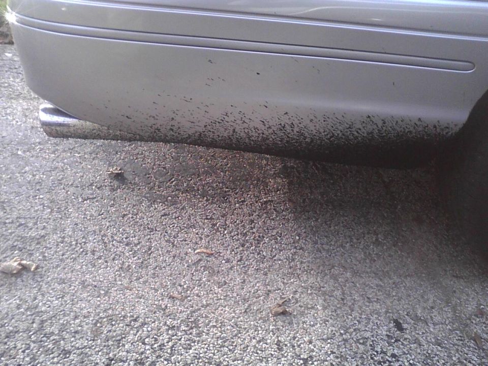 Rear bumper and exhaust pipe of a silver car covered in mud splatters