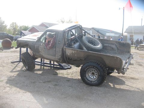 1987 Jeep Comanche - Mud-covered 1987 Jeep Comanche pickup truck with roll cage and spare tire in bed.