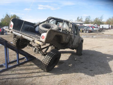 1987 Jeep Comanche - A heavily modified pickup truck is positioned on a ramp in an outdoor lot with other vehicles visible.