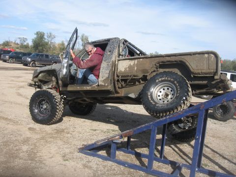 1987 Jeep Comanche - A man sits in a heavily modified and mud-splattered 1987 Jeep Comanche as it rests on a ramp.