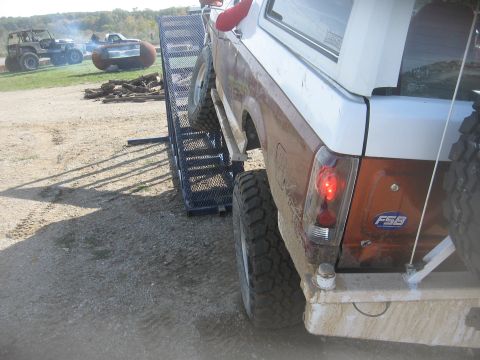 1987 Jeep Comanche - A lifted Ford Bronco II is positioned on a loading ramp, with other vehicles visible in the distance.