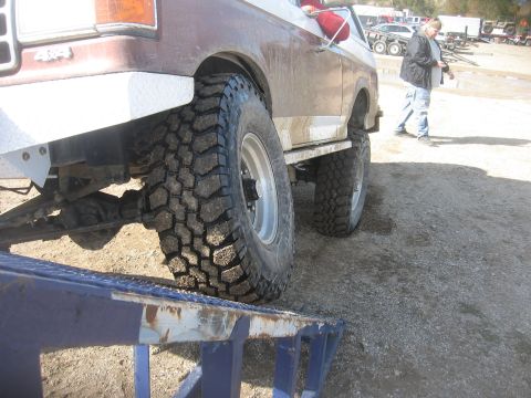 1987 Jeep Comanche - A brown pickup truck with large off-road tires is positioned on a metal ramp, with other vehicles visible in the background.