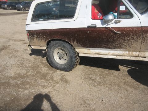 1987 Jeep Comanche - Muddy SUV side view with other vehicles in the background.