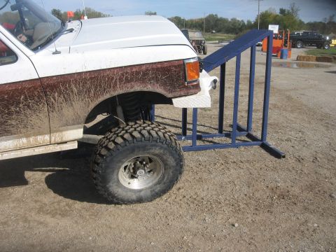 1987 Jeep Comanche - A lifted pickup truck is parked next to a ramp, with other vehicles visible in the background.