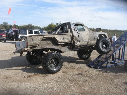1987 Jeep Comanche - A heavily modified Jeep pickup truck navigates an obstacle course, covered in mud.