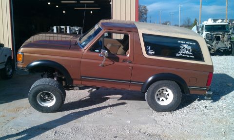 1987 Ford Bronco - Brown 1987 Ford Bronco lifted with a tan removable top. Another vehicle is partially visible in the background.