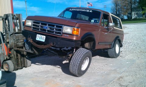 1987 Ford Bronco - A lifted Ford Bronco is being moved by a forklift in an outdoor lot.