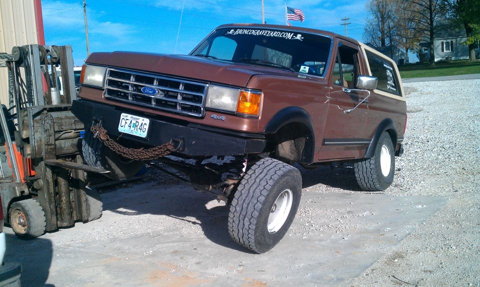 Brown Ford Bronco with lifted suspension and large tires, being lifted by a forklift