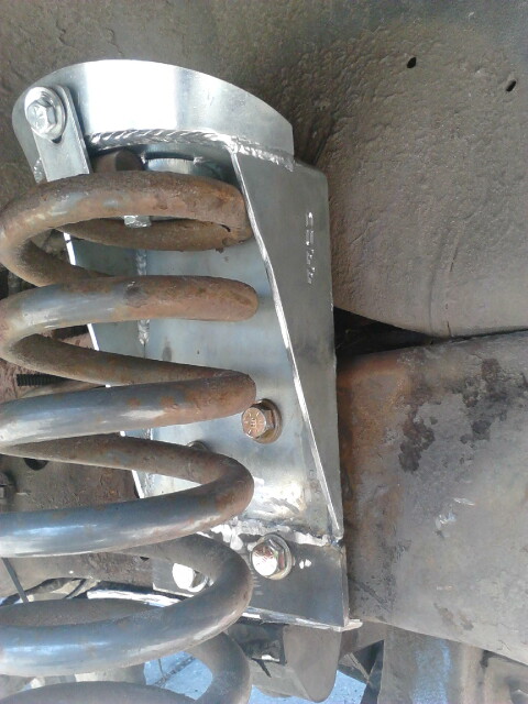 1996 Ford Bronco - Close-up under a truck of a bare, freshly welded steel coil spring retainer/bucket bracket bolted to the frame rail, with visible weld bead…