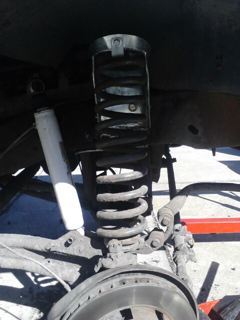 1996 Ford Bronco - Underside view of a lifted 4x4 front suspension, showing a black-painted coil spring seated in the frame spring pocket above the radius arm…