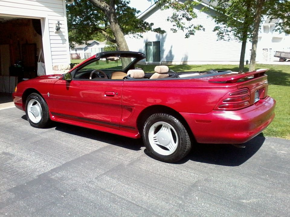 Red 1995 Ford Mustang convertible parked in a driveway next to a garage
