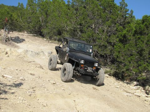 1995 Ford Bronco - A black Jeep Wrangler navigates a challenging off-road course with steep inclines and rocky terrain.
