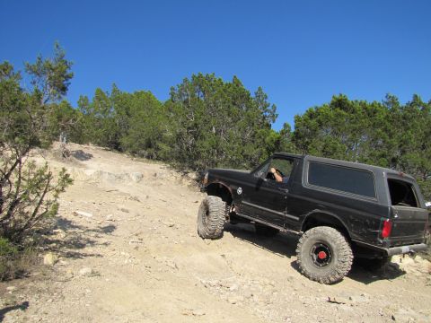 1995 Ford Bronco - A black 1995 Ford Bronco navigates a challenging off-road trail under a clear blue sky.