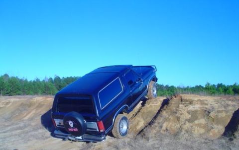 1986 Ford Bronco - A dark blue 1986 Ford Bronco navigates a steep dirt incline under a clear blue sky.