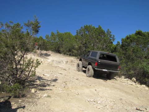 1995 Ford Bronco - 1995 Ford Bronco navigating an off-road trail with large tires and a lifted suspension.