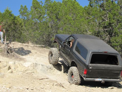 1995 Ford Bronco - A black Ford Bronco navigates a challenging off-road trail with steep rocky terrain.