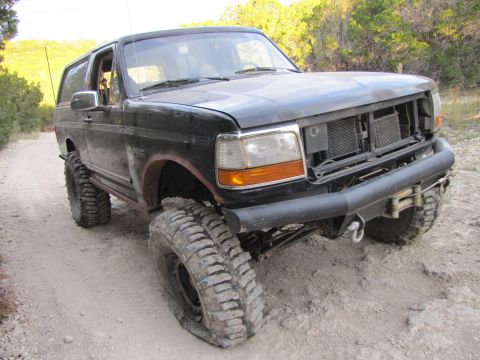 1995 Ford Bronco - Modified 1995 Ford Bronco with large tires and aftermarket bumper on a dirt trail.