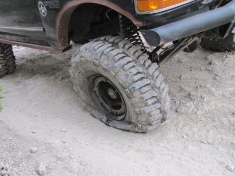 1995 Ford Bronco - A vehicle with a flat tire is parked on a dirt surface, showing the Bronco emblem on its side.