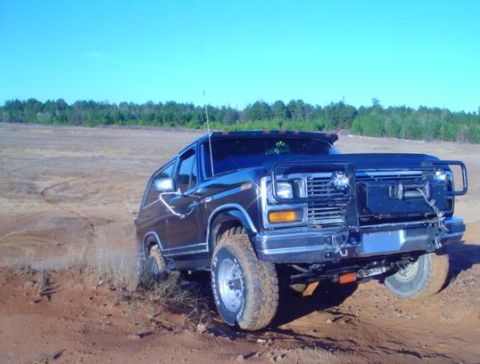 1986 Ford Bronco - This Ford Bronco is navigating a sandy, off-road terrain under a clear blue sky.