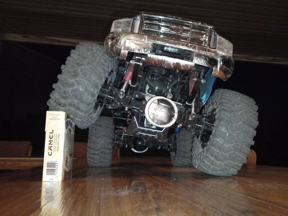 Remote control monster truck with large tires and chrome grille, next to a pack of cigarettes
