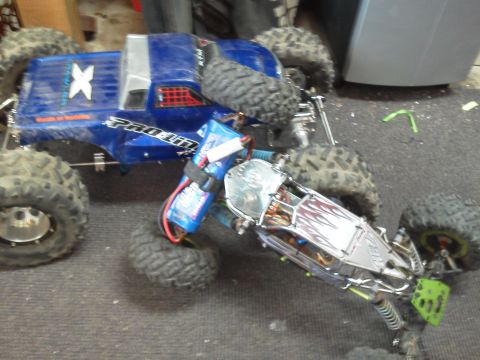 1985 Ford Bronco - Two RC monster trucks are positioned on a carpeted surface, one appears to be partially on top of the other.