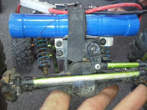 1985 Ford Bronco - Close-up view of a modified remote control car's undercarriage, highlighting its battery and suspension components.