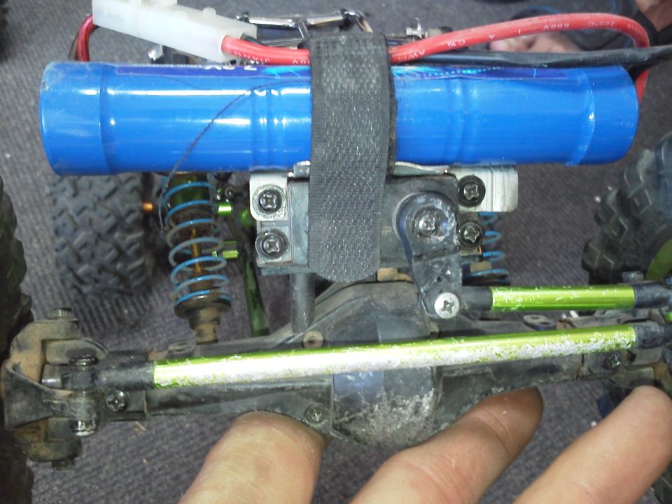 Remote control car chassis with blue battery pack, green suspension arms, and visible steering mechanism