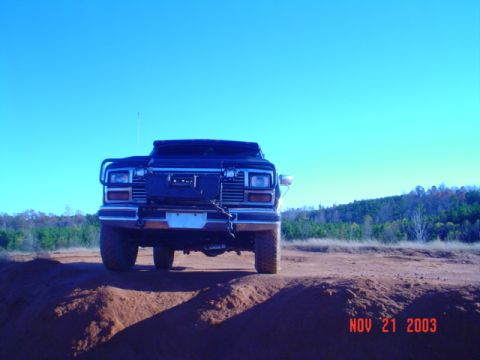 1986 Ford Bronco - This 1986 Ford Bronco is captured from the front, navigating a dirt track under a clear blue sky.
