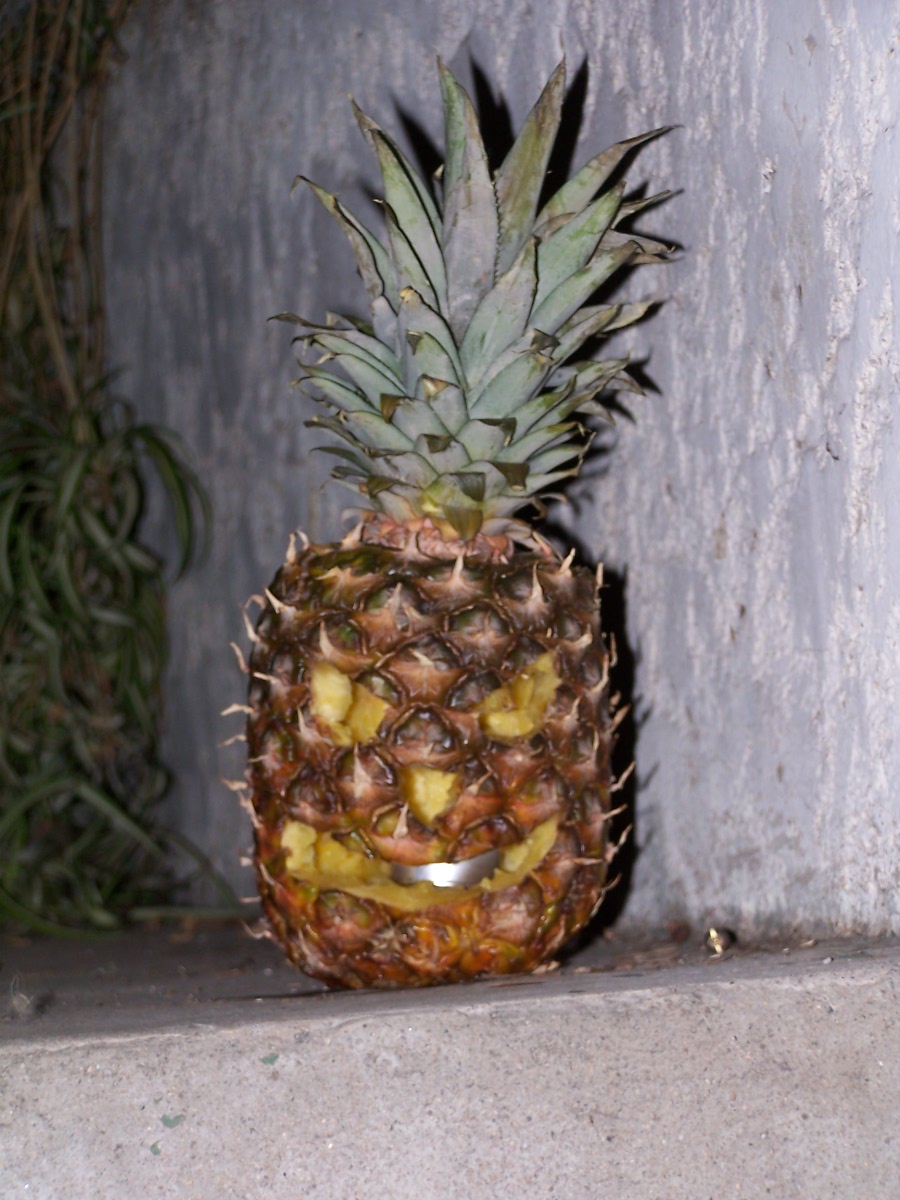 Carved pineapple with a face, lit from within, resting on a concrete ledge