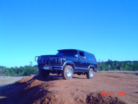 1986 Ford Bronco - This SUV is parked on a dirt mound with trees in the background.