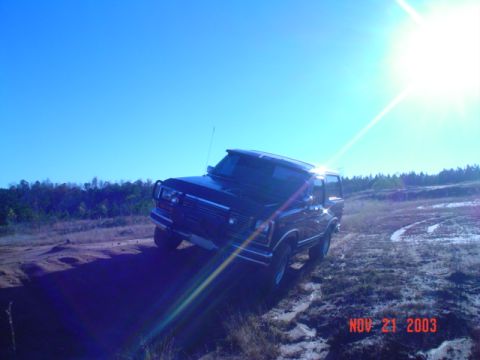 1986 Ford Bronco - This 1986 Ford Bronco is captured in a three-quarter front view while navigating a dirt path under a bright sun.