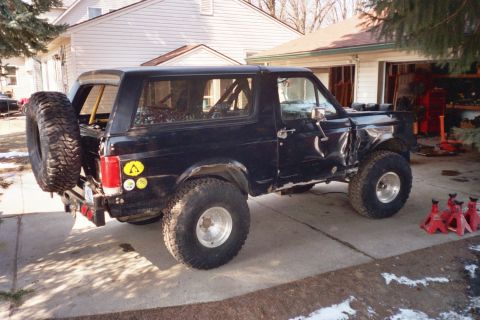 1988 Ford Bronco - This black 1988 Ford Bronco features off-road tires, a spare tire mounted on the rear, and an interior roll cage.