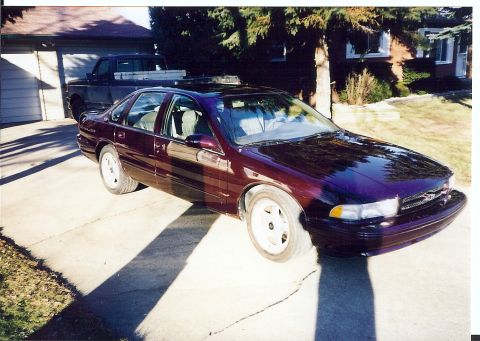 1988 Ford Bronco - Dark purple 1995 Chevrolet Impala SS parked in a driveway with a pickup truck behind it.