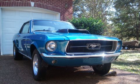 1967 Ford Mustang - A blue 1967 Ford Mustang coupe with a hood scoop sits in a driveway near a garage.