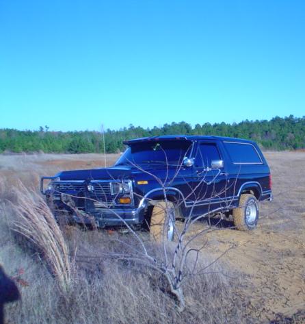 1986 Ford Bronco - This dark blue SUV, likely from the early 1980s, is parked in a dry, grassy field under a clear blue sky.