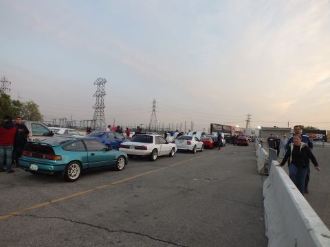 2003 Ford Crown Victoria - Vehicles queued along a track staging lane at dusk beneath power line towers.