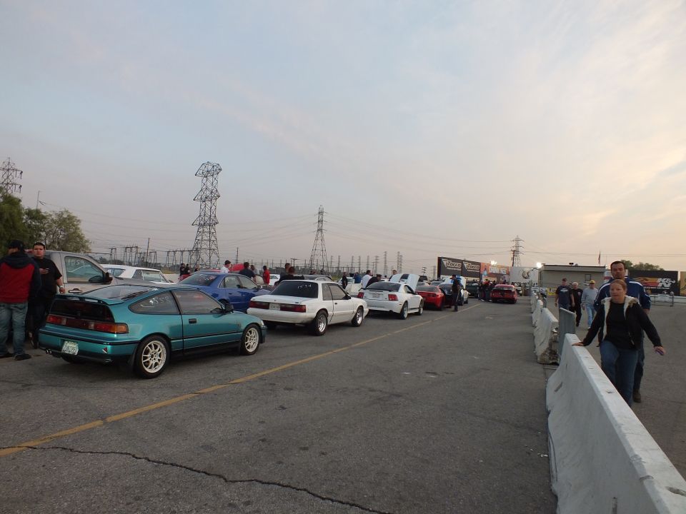 Line of cars at dusk drag strip staging lane including teal Honda CRX and Mustangs