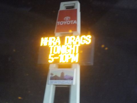 2003 Ford Crown Victoria - Illuminated event sign announcing NHRA drag racing hours below a Toyota badge.