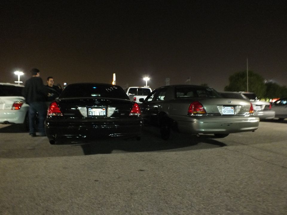 Rear of black Crown Victoria with plate FYTLVTC beside green sedan in night lot
