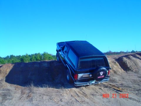 1986 Ford Bronco - 1986 Ford Bronco navigating a sandy incline, spare tire cover visible.