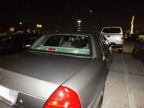 2003 Ford Crown Victoria - Gray Crown Victoria rear three-quarter, 1624 marked on the back glass, white Ford pickup alongside
