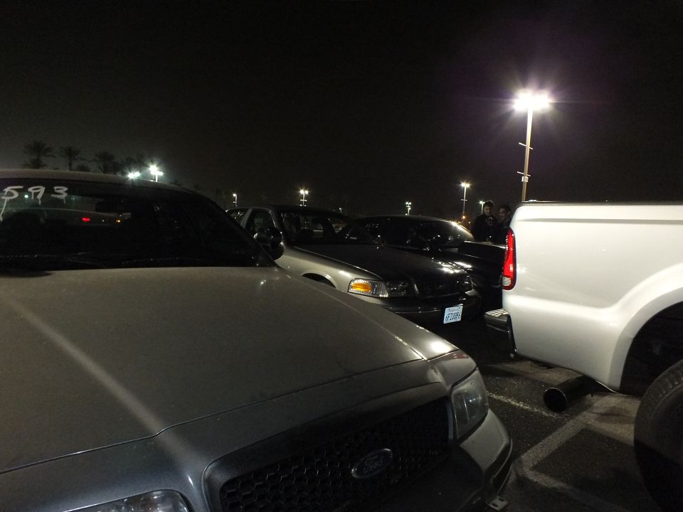 Ford trucks and Crown Victoria sedans parked in a dark lot, white pickup at right